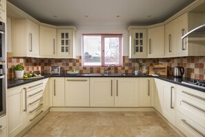 A kitchen with beige cabinets, a black countertop, a window with blinds, and a tiled backsplash.