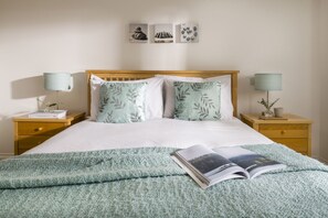 A neatly made bed with a green blanket and pillows, two bedside tables with lamps, and a wall with three framed pictures.