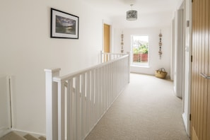 A hallway with a white railing, a framed picture on the wall, and a basket on the floor. - Rock House - sleeps 8 guests  in 4 bedrooms (Bude)