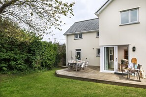 A two-story house with a patio, a lawn, and a garden.