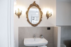 Een badkamer met een wit wastafelmeubel, een spiegel met gouden lijst en wandlampen.