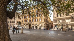 Une rue bordée d’immeubles, avec un arbre et des piétons.