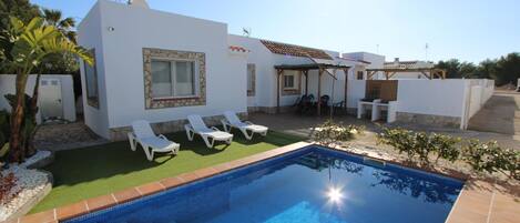 A modern house with a swimming pool, white walls, and a patio area with lounge chairs.