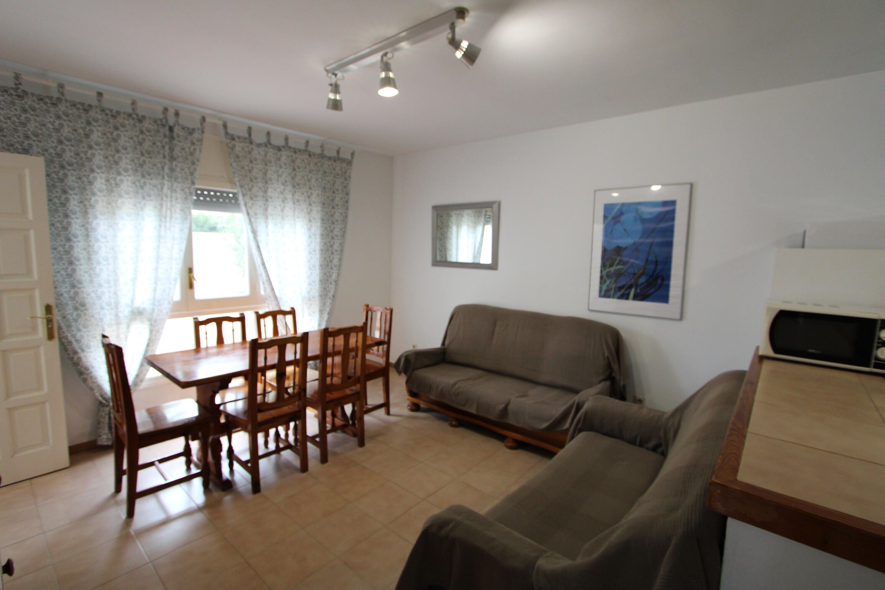 A living room with a sofa, a dining table with chairs, a television, and a window with curtains.