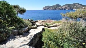 Un sentier côtier qui mène à une zone rocheuse offrant une vue sur la mer et les collines lointaines.