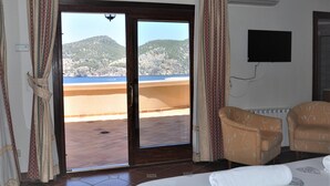 Une chambre d’hôtel comprenant un lit, deux fauteuils, un téléviseur et un balcon avec vue sur une plage et des montagnes.