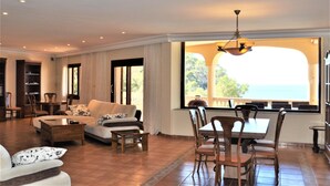 Un salon spacieux comprenant un canapé, une table basse et un coin repas avec des chaises. Une grande fenêtre offre une vue sur l’extérieur.