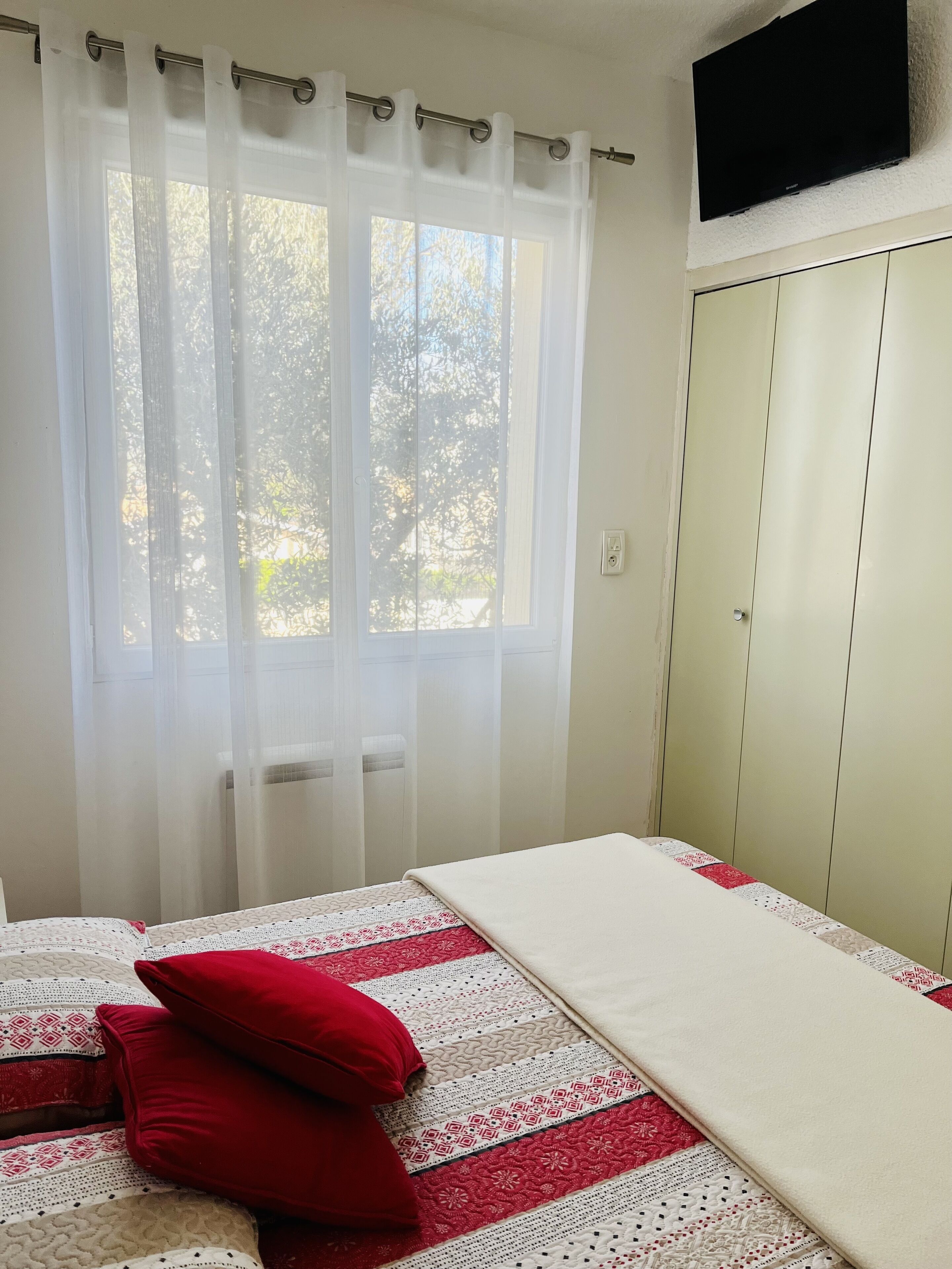 A bedroom with a bed, a wardrobe, and a window with sheer curtains.