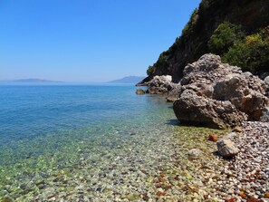 A clear coastal beach with rocky terrain and a calm sea.