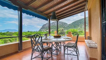Enjoy al fresco dining on the terrace with a round table and wicker chairs, surrounded by lush greenery and distant mountains.