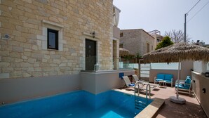 Un edificio de piedra con piscina, mobiliario exterior y una estructura de techo de paja.
