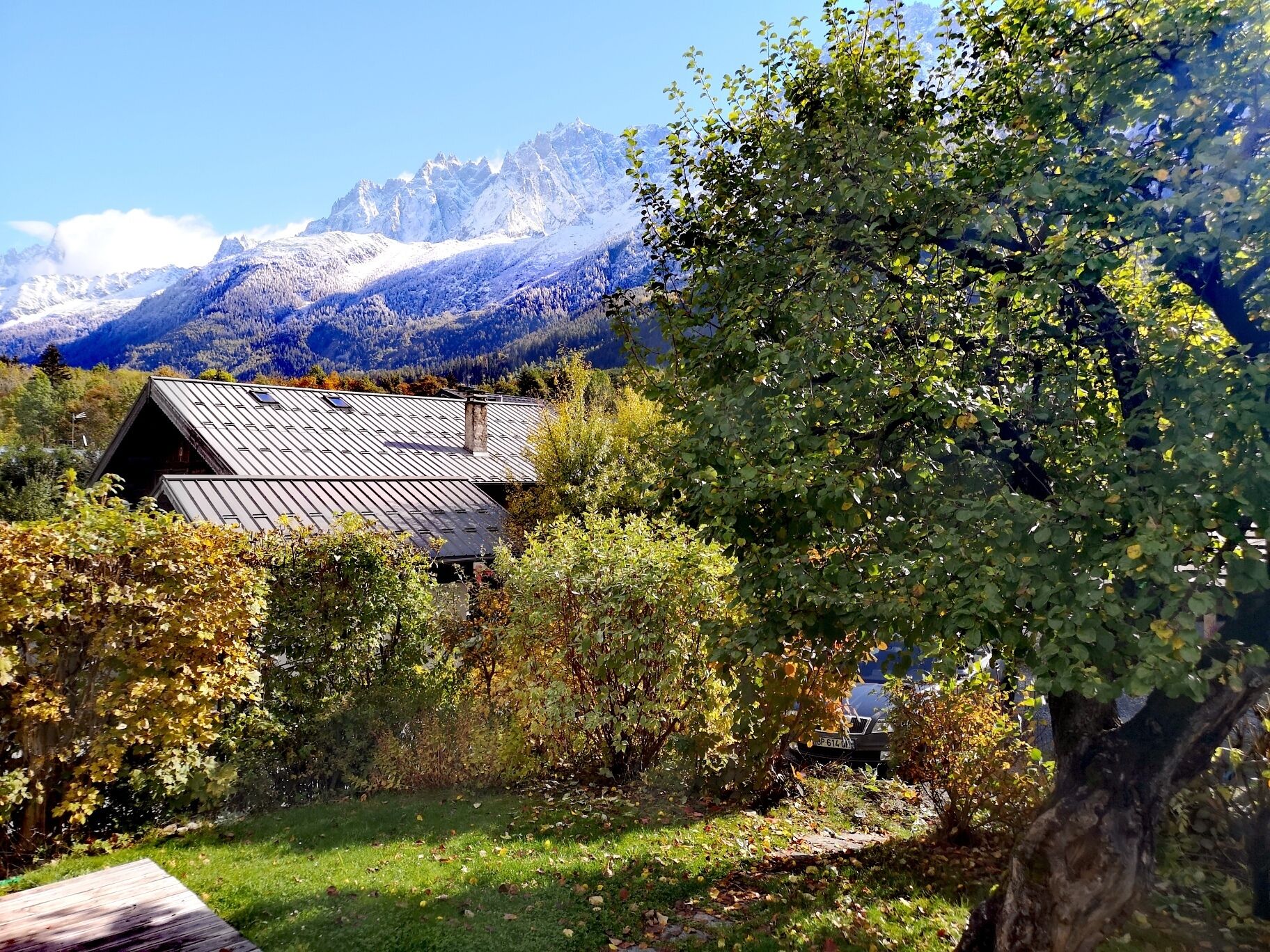 Ein rustikales Blockhaus mit geneigtem Dach, umgeben von üppiger Vegetation und einer Bergkulisse.