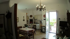Een ruime woonkamer met een eethoek, een keuken en een schuifpui naar een terras.