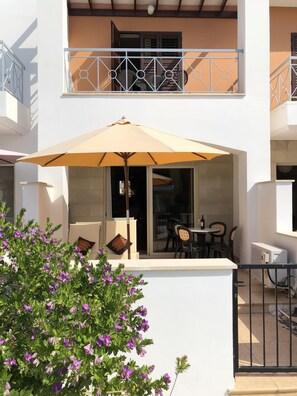 An outdoor patio with a table and chairs, a large umbrella, and a view of the building's interior. - Beautiful Holiday Villa With Pool In Tombs Of The Kings Area . Sleeps 4 .  (kato Paphos)