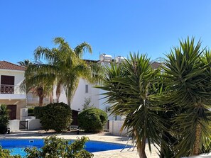 A pool area with a clear blue pool, surrounded by palm trees and a white building with balconies. - Beautiful Holiday Villa With Pool In Tombs Of The Kings Area . Sleeps 4 . (kato Paphos)