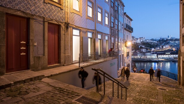 A nighttime urban scene with a cobblestone street, buildings with patterned facades, and a river in the background.