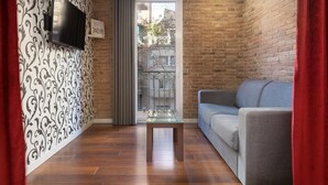 A living room with a brick wall, a grey sofa, a glass coffee table, and a TV mounted on the wall.
