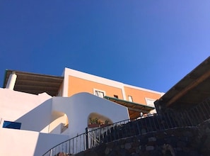 A building with a white facade and orange trim, featuring a stone staircase and a balcony with potted plants. - Didyme - Comfortable flat on the beach with terrace and island views - Wifi (Lipari)