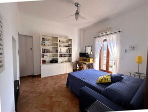 A bedroom with a bed, a desk with a chair, a bookshelf, and a window with curtains.