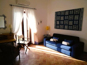 A living room with a blue sofa, a wooden desk, a chair, a lamp, and a patterned wall hanging. - Didyme - Comfortable flat on the beach with terrace and island views - Wifi (Lipari)