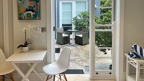 Quarto com uma mesa branca, uma cadeira branca, um vaso com planta e um quadro colorido na parede.