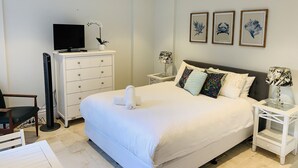 Um quarto com uma cama grande, penteadeira, televisão e obras de arte na parede.