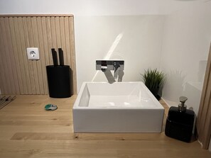 Een moderne badkamer met een rechthoekig wastafelmeubel, een zwarte prullenbak, een groene tandenborstel en een potplant.