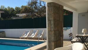 A poolside area with lounge chairs, a stone pillar, and a table with towels and a hat.