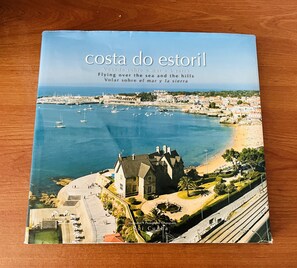 Boekomslag met de titel “Costa do Estoril”, met een luchtend view van een kustplaatsje, inclusief een strand, jachthaven en een opvallend gebouw.
