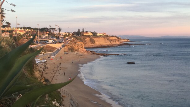 A coastal beach with a paved walkway and a rocky cliff.