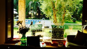 A room with a view of a garden, a table with a vase of flowers, and a chair. - Otranto: SPLENDID TENUTA WITH POOL AND TENNIS COURSE. (Muro Leccese)