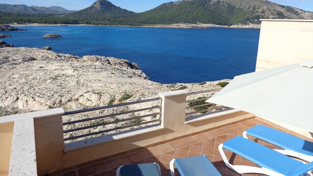 Une terrasse offrant une vue sur la mer et les montagnes, avec une table et deux fauteuils bleus confortables.