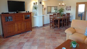 Un salon comprenant un téléviseur, un meuble en bois, une table à manger avec des chaises et un canapé.