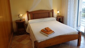 Une chambre avec un lit en bois, une table de chevet avec une lampe, une fenêtre avec des rideaux et une vue sur le balcon.
