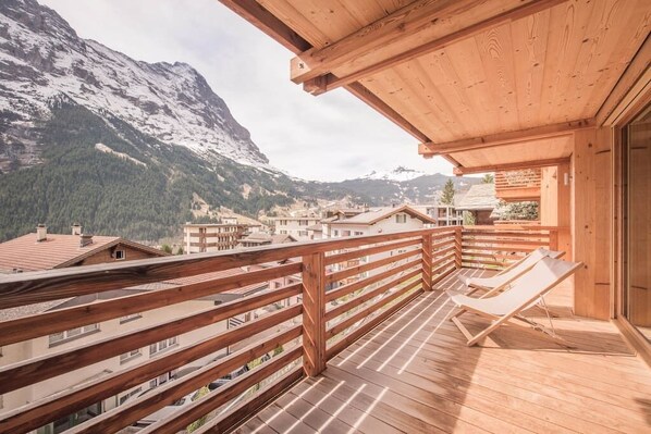A wooden balcony with a view of snow-capped mountains and a village below. - Central gem with uninterrupted views (Grindelwald)