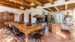 Un'ampia cucina con un grande tavolo e sedie in legno, un camino e un'area pranzo con un divano in vimini.