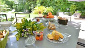 Ein Tisch im Freien mit verschiedenen Speisen, darunter Obst, Brot und ein Glas mit Blumen.