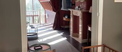 A room with a wooden chair and a table, a television, a mirror, and a window with curtains.