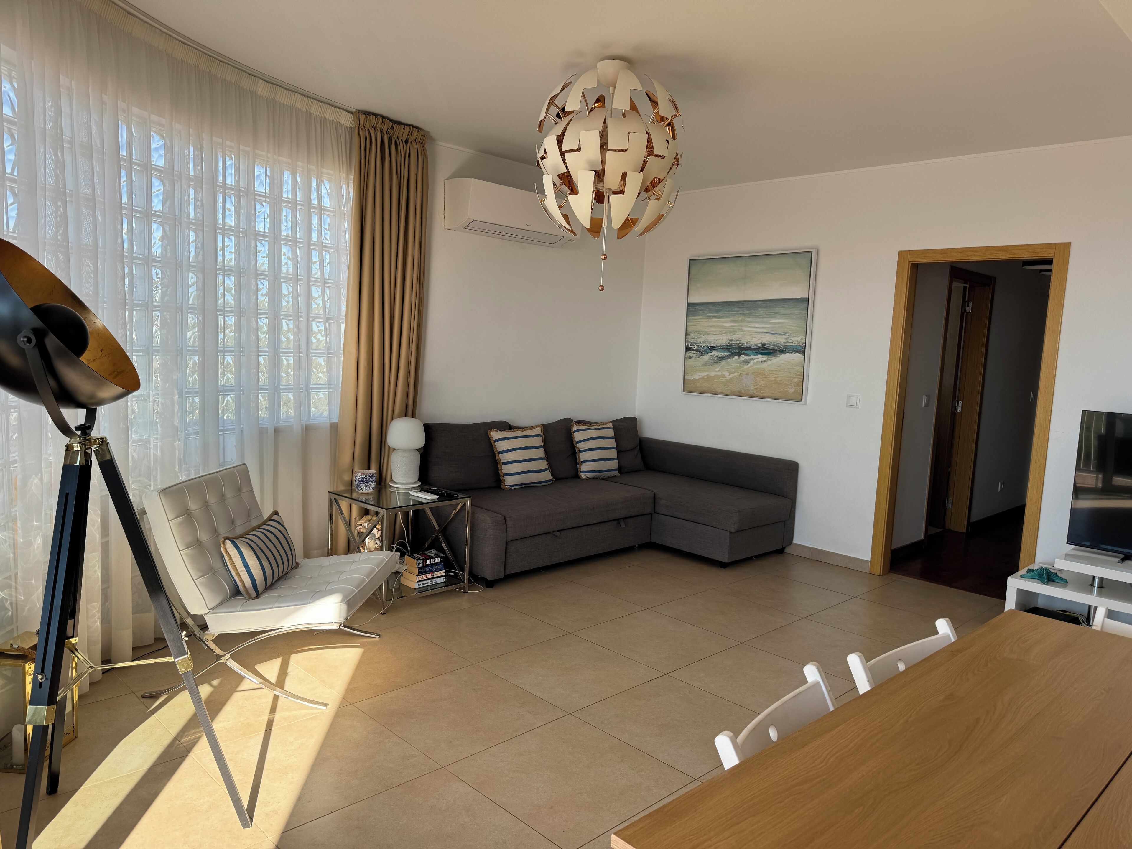 Uma sala de estar moderna com um sofá seccional, uma mesa de jantar e uma luminária de teto esférica e diferenciada.