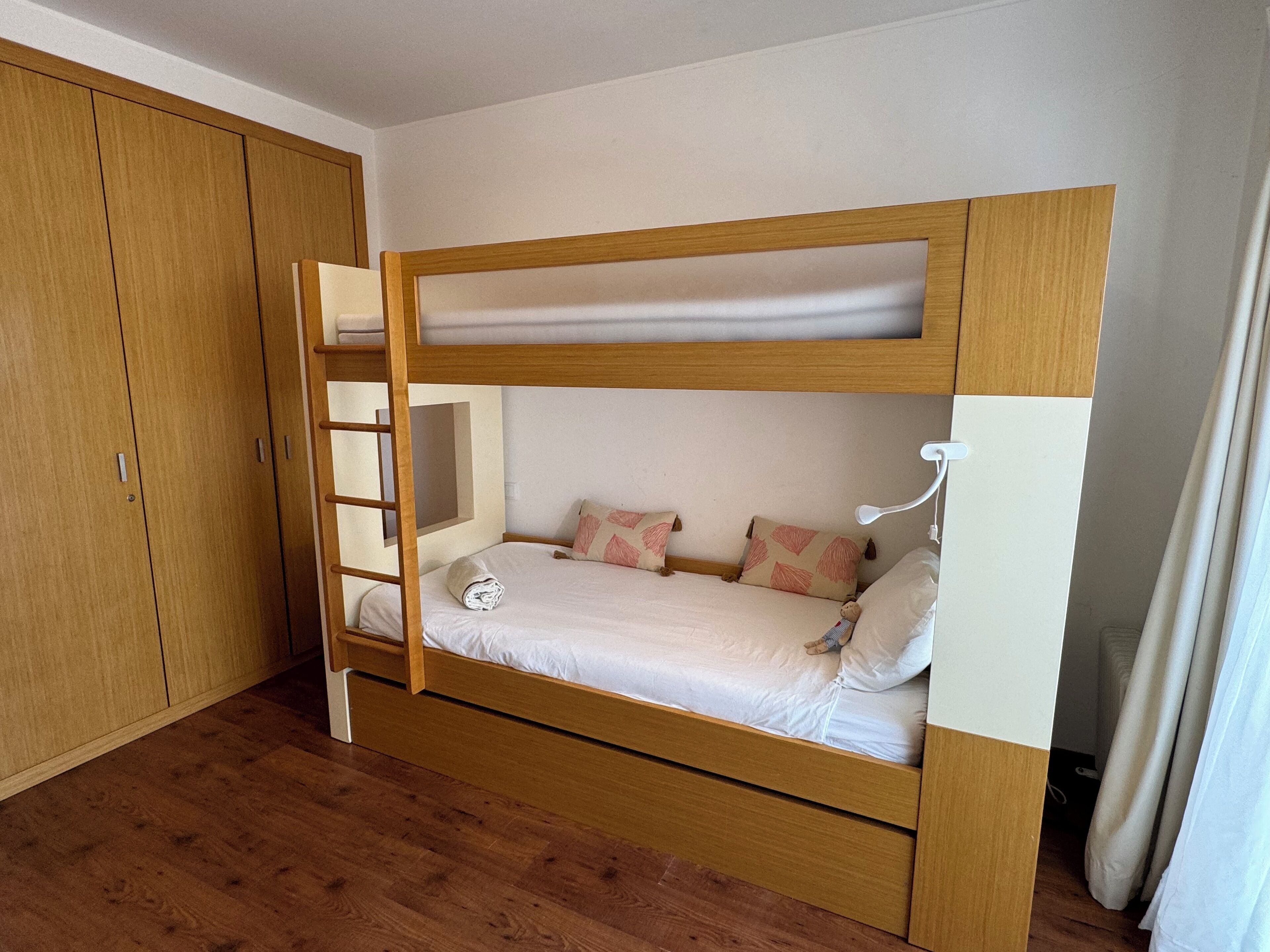 Ein Etagenbett mit Holzrahmen, einem kleinen Fenster und einer weißen Wand.