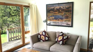 Una sala de estar con un sofá, dos cojines estampados, una mesa de centro de madera y un cuadro enmarcado de las montañas Cairngorm.
