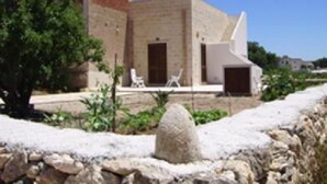 A building with a stone facade, a flat roof, and a small porch area with chairs. - House / Villa - FAVIGNANAHouse with garden (Favignana)