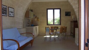 A cozy room with a bed, a dining table with chairs, a kitchen area, and a large window. - House / Villa - FAVIGNANAHouse with garden (Favignana)