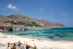Una playa con agua turquesa cristalina, una orilla arenosa y montañas al fondo.