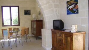 A dining area with a table and chairs, a television on a wooden cabinet, and a stone wall. - House / Villa - FAVIGNANAHouse with garden (Favignana)