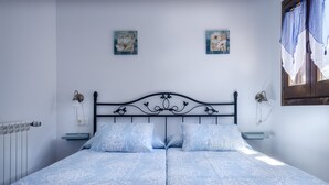 A double bed with a patterned bedspread, two wall-mounted lamps, and two framed floral artworks on the wall.
