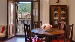 A dining area with a round table, chairs, a chandelier, and a view of a balcony with a stone roof.