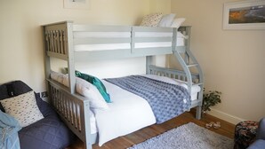 Ein Etagenbett mit weißer Matratze, einer grauen Decke und gemusterten Kissen. Auf dem Boden liegt ein grauer Teppich und neben dem Bett steht eine kleine Pflanze.