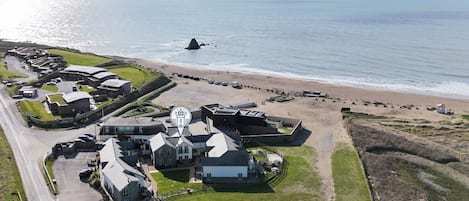 An aerial view of a coastal property with multiple buildings, a parking area, and a beach.