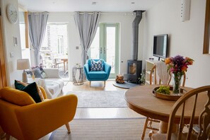 A living room with a sofa, a blue armchair, a dining table with chairs, a TV, and a fireplace.